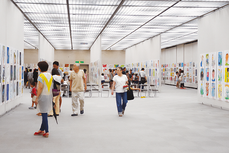 絵が並ぶ展示会場を歩く人たち